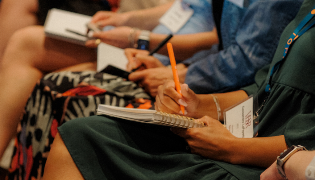 Close-up of people writing in notebooks during a conference.
